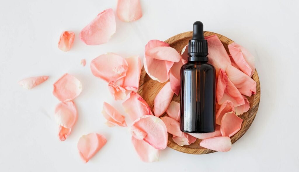 Top view of empty brown bottle for skin care product placed on wooden plate with fresh pink rose petals on white background isolated